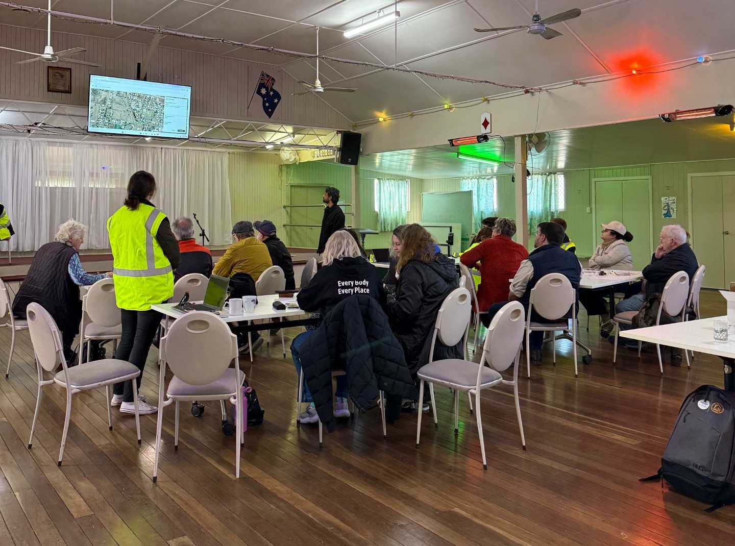 Image of a workshop in progress, with people at multiple tables viewing a presentation on a screen. Taken at the Westbrook Hall.